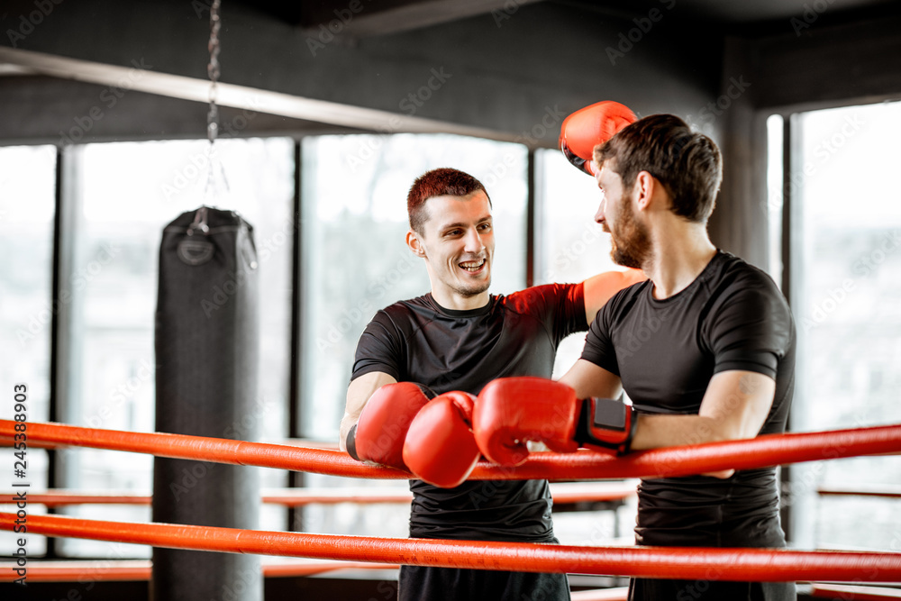 Two athletic men in black sportswear talking together, having fun during the break on the boxing ring at the gym