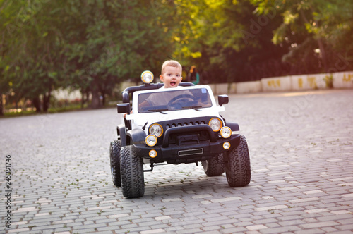 Cute 2 year old boy in a white T shirt is riding a white electric car in the park photo
