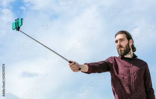 A man stands taking a self portrait using a selfie stick