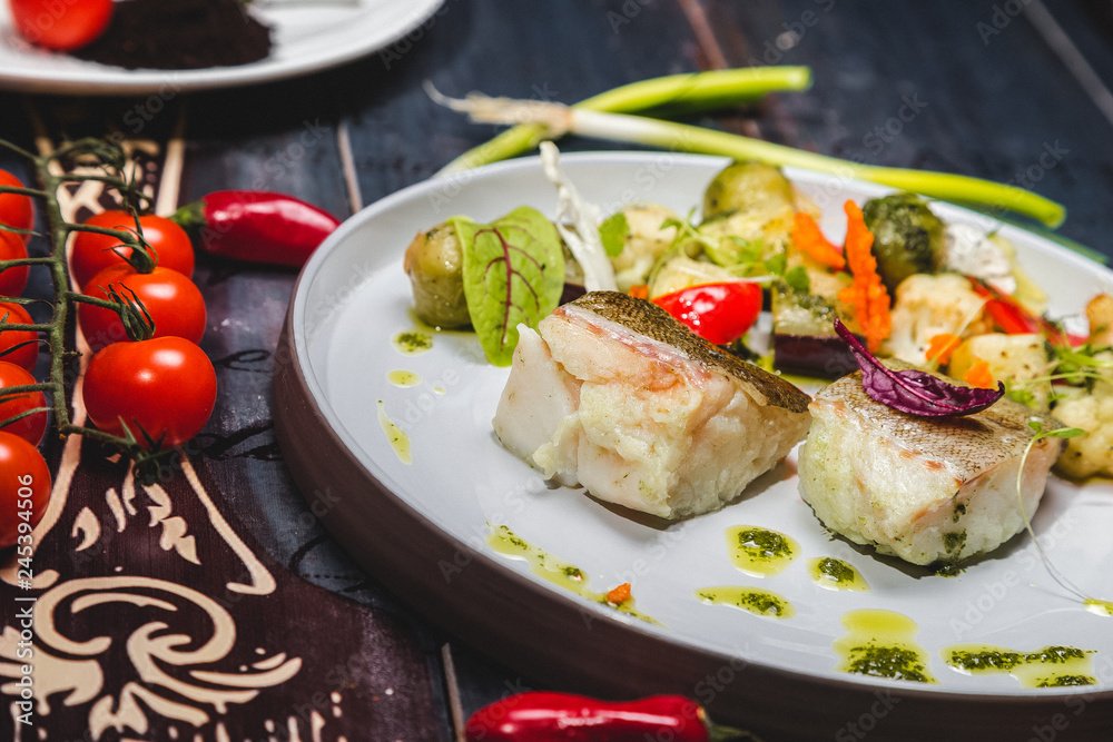 fish with steamed vegetables on a white plate. wooden background decorated with vegetables fish with steamed vegetables on a white plate. wooden background decorated with vegetables