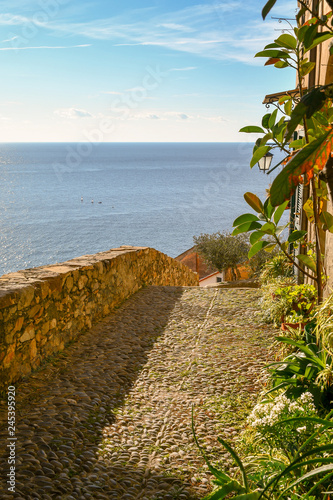 Narrow cobblestone alley of the medieval village of Cervo Ligure with view on the sea, LIguria, Italy