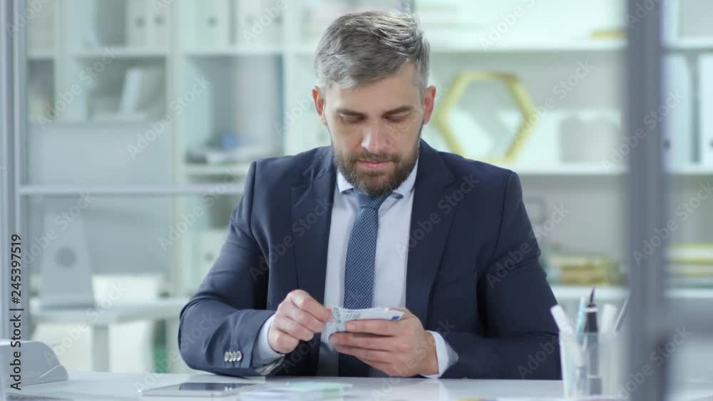 Tracking shot of middle aged Caucasian businessman counting euro banknotes and using calculator on digital tablet while working at office desk Tracking shot of middle aged Caucasian businessman counting euro banknotes and using calculator on digital tablet while working at office desk