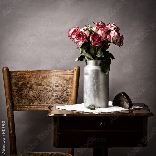 fading bouquet of flowers, in old milk can on old side table in vintage mood