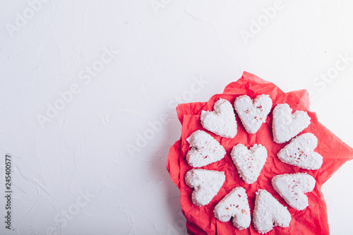 White heart shaped Valentine's day cookies with white glaze and coconut flakes on a red napkin. Copy space. Flat lay