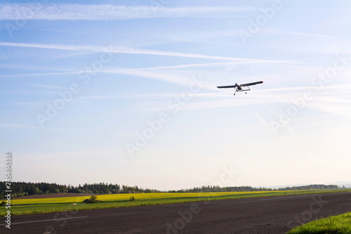 Unmanned aerial vehicle surveillance drone with light and camera landing on airport runway, ground, airfield, sunny summer morning, drone delivery concept, copy space on clear sky