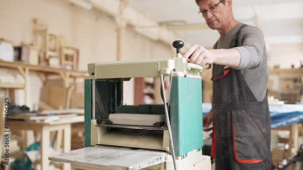 Experienced professional furniture maker using woodworking machine for sanding wooden plank in his workshop Experienced professional furniture maker using woodworking machine for sanding wooden plank in his workshop
