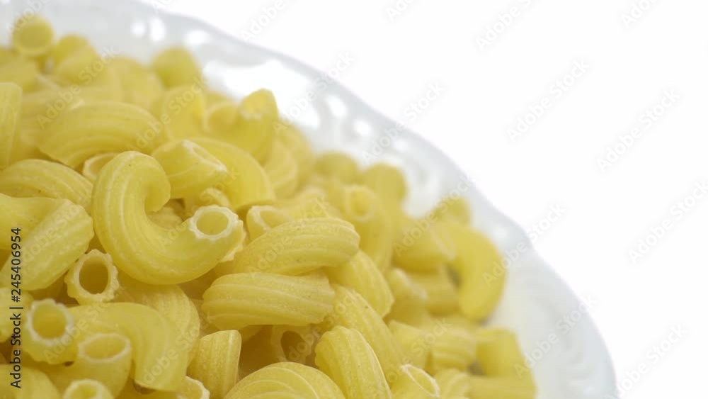 Raw macaroni in rotation. Elbow macaroni.  Macaroni rigati close up.  Raw pasta  isolated on white. Italian cuisine concept.