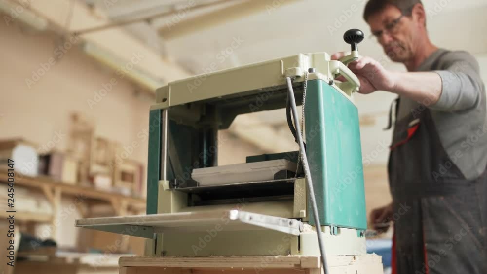 Professional furniture maker measuring wooden plank and sanding it with woodworking machine in his workshop Professional furniture maker measuring wooden plank and sanding it with woodworking machine in his workshop