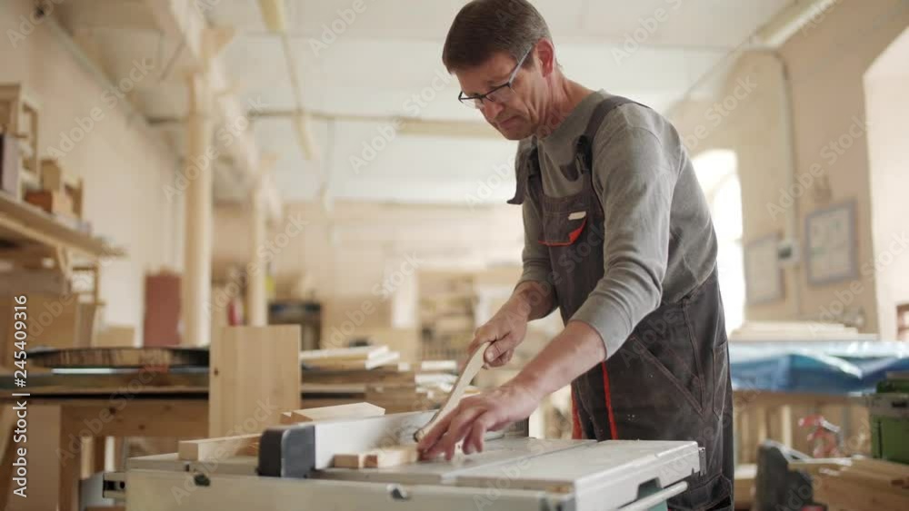 Medium shot of mature carpenter using circular saw for cutting pieces of wood in his woodworking workshop Medium shot of mature carpenter using circular saw for cutting pieces of wood in his woodworking workshop