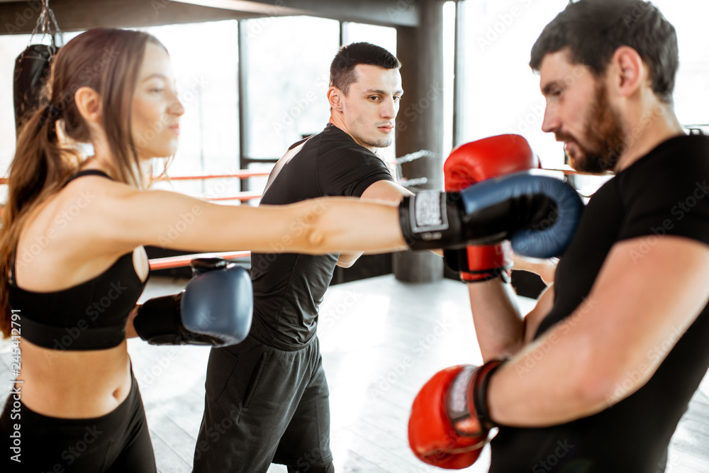 Fototapeta Man and woman training to box with personal coach on the boxing ring at the gym