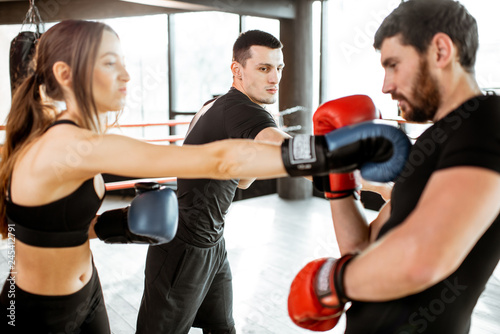 Man and woman training to box with personal coach on the boxing ring at the gym