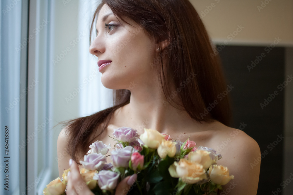 Beautiful happy woman looking at the window out of the bedroom with a bouquet of flowers. Spring concept Beautiful happy woman looking at the window out of the bedroom with a bouquet of flowers. Spring concept
