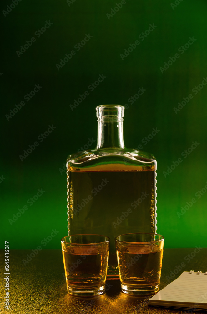 Bottle and glasses of whiskey on a green background near the phone. Bottle and glasses of whiskey on a green background near the phone.