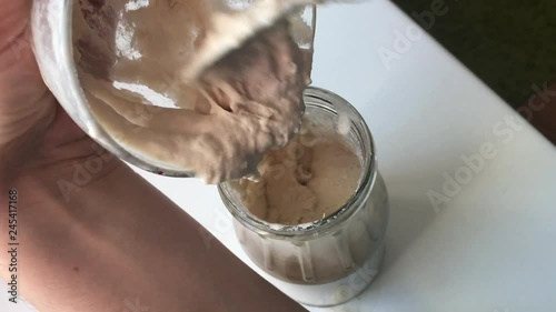 A woman adds a mixture of water and flour to a fermenting ferment for feeding.
