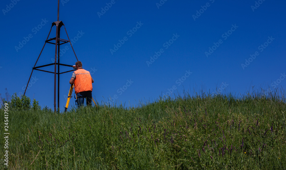 Professional Male Land Surveyor Measures Ground Control Point Using a GPS Rover. Green Field on a Background.. Professional Male Land Surveyor Measures Ground Control Point Using a GPS Rover. Green Field on a Background..