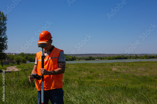 Professional Male Land Surveyor Measures Ground Control Point Using a GPS Rover. Green Field on a Background