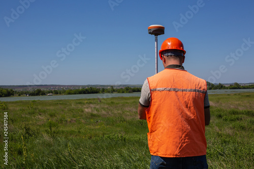 Professional Male Land Surveyor Measures Ground Control Point Using a GPS Rover. Green Field on a Background