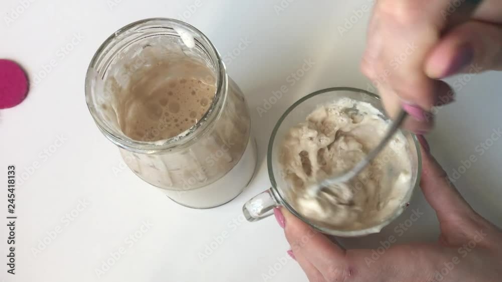 A woman is mixing flour in a glass with water. Makes a mixture for feeding bread sourdough. Sourdough stands next to a glass jar. A woman is mixing flour in a glass with water. Makes a mixture for feeding bread sourdough. Sourdough stands next to a glass jar.