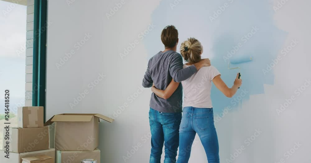 Cute couple painting wall in new home together, happy new homeowners, home painting
