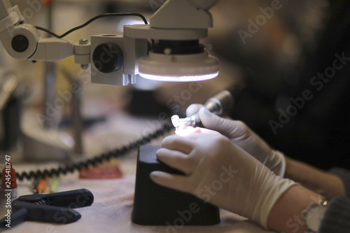 The hands of a dental technician processing a prosthesis with a drill under the microscope photo