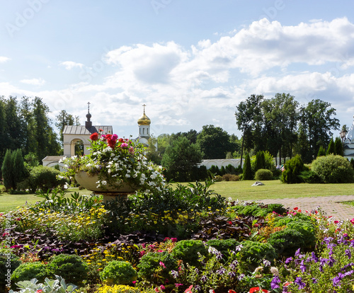 Greenery floral historical monastery garden with colorful spring summer flowers, trees and old church buildings