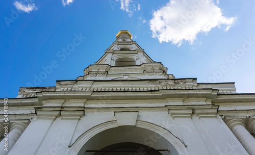 Old historical white church tower building with golden shiny top located in a monastery from bottom in a summer spring day with blue sky and white clouds 