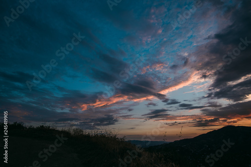 Dramatic purple and orange cloudy sunset with blue sky over mountain silhouette © Katherine