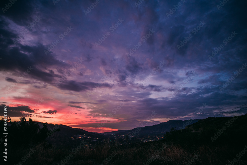 Dramatic pink and purple cloudy sunset with blue sky over mountain silhouette