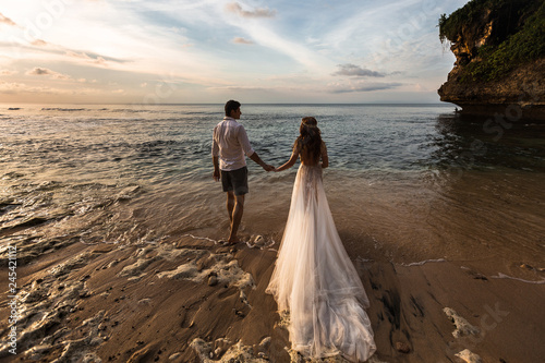 Bride and groom go to sea on the beach at sunset