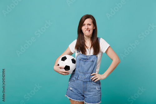 Worried nervous young woman football fan support favorite team with soccer ball biting lips isolated on blue turquoise background. People emotions, sport family leisure concept. Mock up copy space. © ViDi Studio