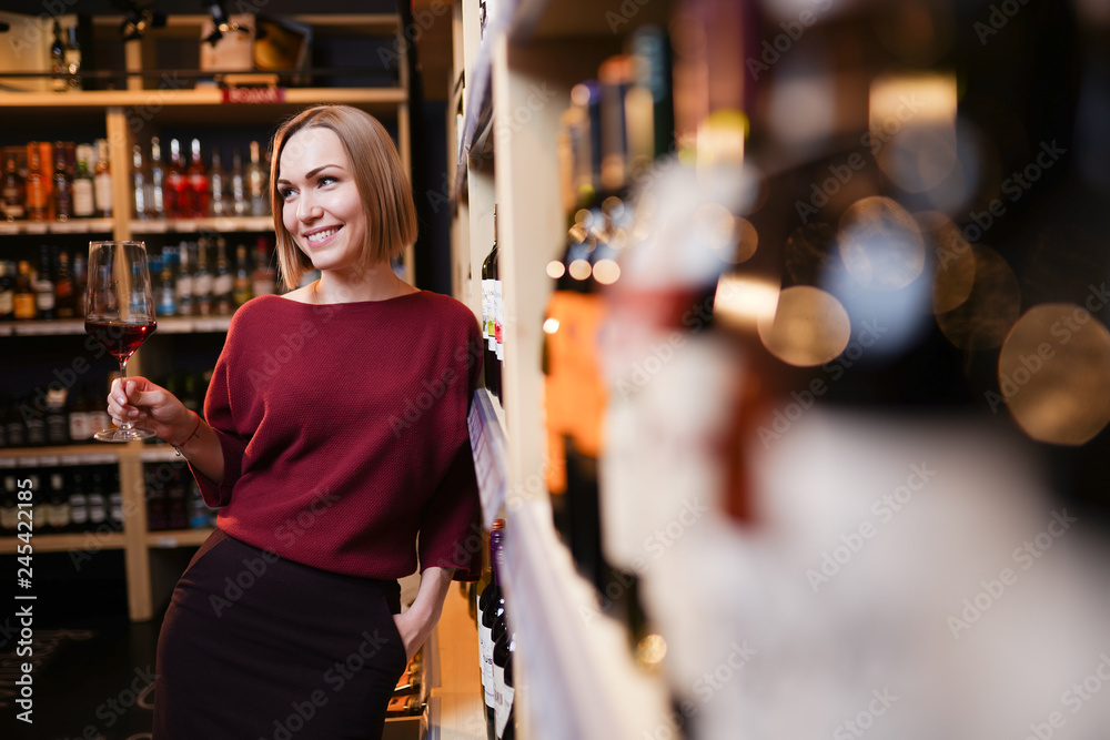 Photo of young woman with wine glass in store on background of shelves
