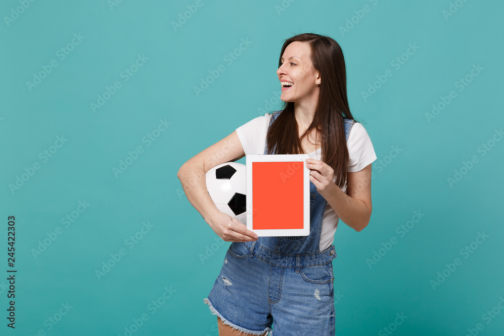 Beautiful woman football fan holding soccer ball, tablet pc computer with blank empty screen isolated on blue turquoise background. People emotions, sport family leisure concept. Mock up copy space. Beautiful woman football fan holding soccer ball, tablet pc computer with blank empty screen isolated on blue turquoise background. People emotions, sport family leisure concept. Mock up copy space.