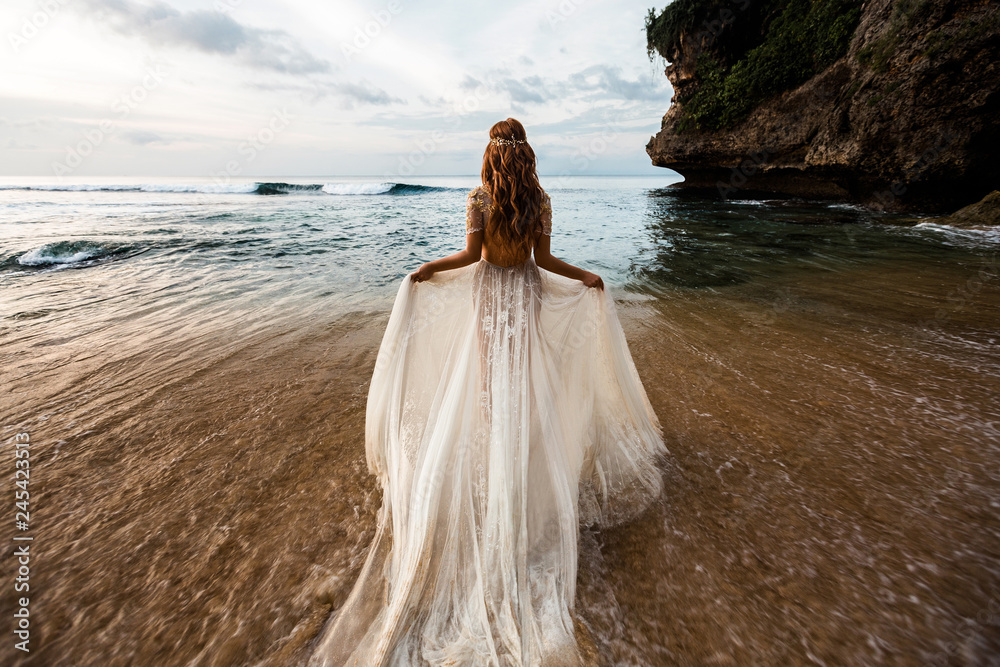 Bride in a white wedding dress comes into the sea water on the beach Bride in a white wedding dress comes into the sea water on the beach