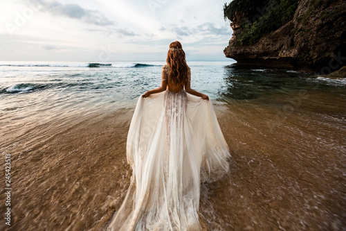 Bride in a white wedding dress comes into the sea water on the beach