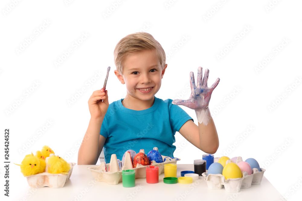 The child is painting Easter eggs. The boy is sitting at a table with colorful paints, his hands are dirty. She is happy, preparing for Easter. White isolated. The child is painting Easter eggs. The boy is sitting at a table with colorful paints, his hands are dirty. She is happy, preparing for Easter. White isolated.