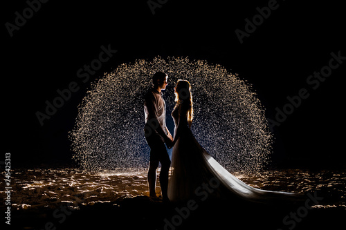 Bride and groom on the night beach against the background of a glowing sand sphere