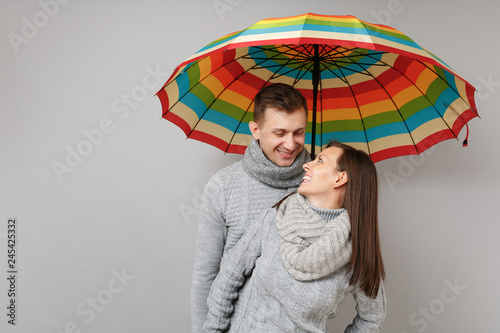 Couple girl guy in gray sweaters scarves together under umbrella isolated on grey wall background, studio portrait. Healthy lifestyle ill sick disease treatment cold season concept. Mock up copy space