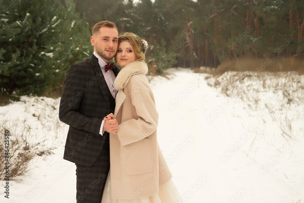 man embraces and holds the hand of a girl. stand in the forest, on the snow, in winter. in a suit and dress with a coat. man embraces and holds the hand of a girl. stand in the forest, on the snow, in winter. in a suit and dress with a coat.