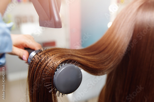 Shine Drying long brown hair with dryer and round brush after Spa treatment. Female master