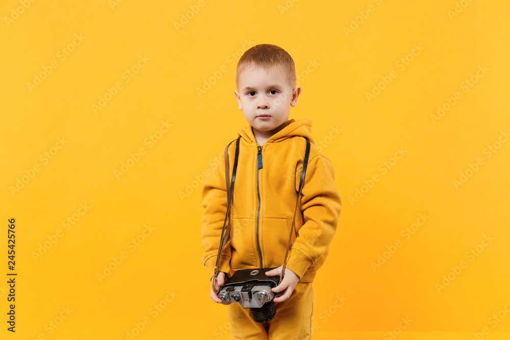 Little kid boy 3-4 years old wearing yellow clothes hold camera isolated on orange wall background, children studio portrait. People sincere emotions, childhood lifestyle concept. Mock up copy space. Little kid boy 3-4 years old wearing yellow clothes hold camera isolated on orange wall background, children studio portrait. People sincere emotions, childhood lifestyle concept. Mock up copy space.