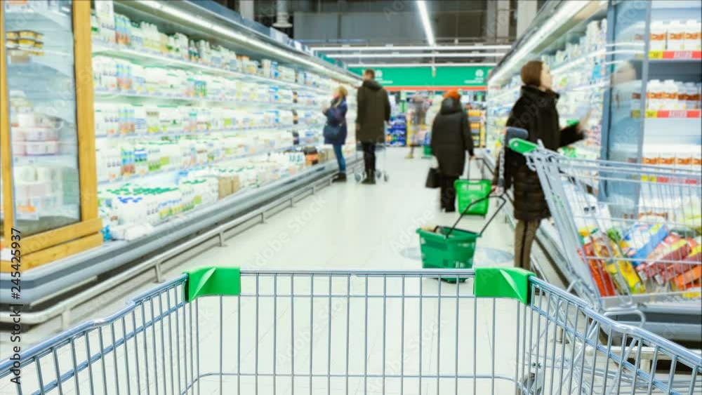 Timelapse - shopping trolley stands on the background of blurred customers in the aisle, people choose products