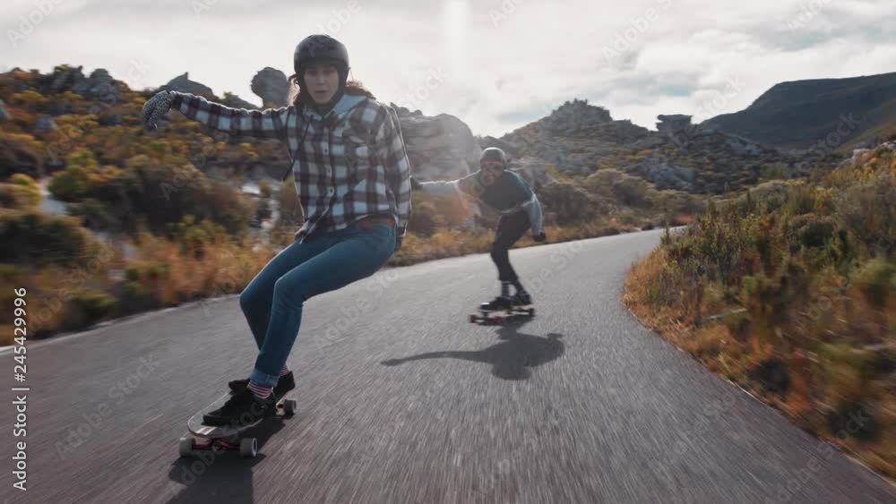 young happy woman riding longboard friends skating enjoying cruising downhill on beautiful countryside road having fun using skateboard wearing protective helmet