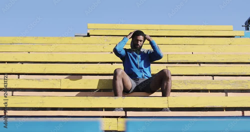 A black male athlete sits in the stands on the stadium in the open air. A black male athlete sits in the stands on the stadium in the open air.
