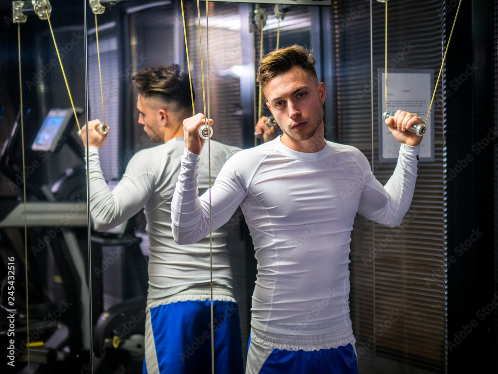 Obraz premium Muscular young man, training shoulders on gym cable machine