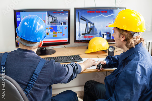 Engineers in the control room, looking at computer monitor.Image of a pump jack at monitor is mine property,mine own work