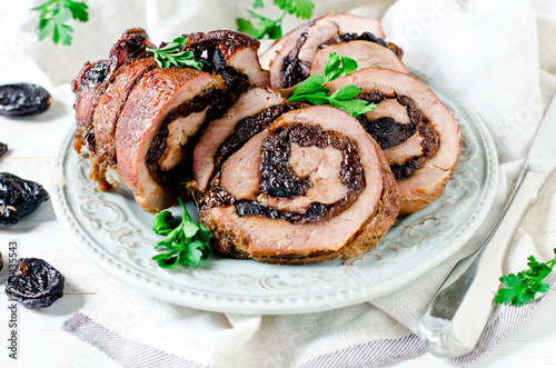 Baked turkey roll with prunes on a plate on a white wooden table