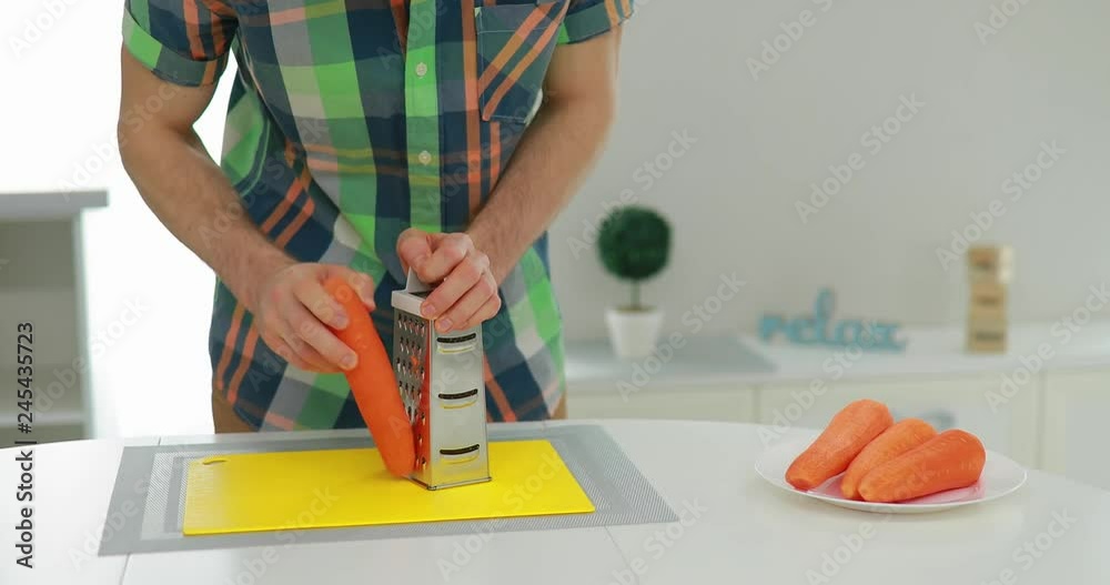 Man grates carrot on stainless steel grater on a cuisine Man grates carrot on stainless steel grater on a cuisine