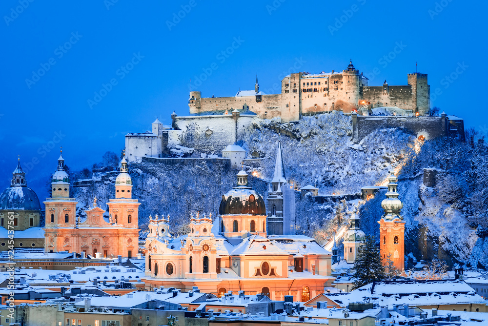 Naklejka premium Salzburg, Austria: Zimowy widok na zabytkowe miasto Salzburg ze słynnym Festung Hohensalzburg i rzeką Salzach oświetloną o pięknym zmierzchu podczas malowniczych świąt Bożego Narodzenia w zimę