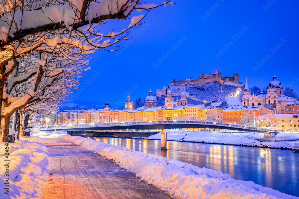 Naklejka premium Salzburg, Austria: Zimowy widok na zabytkowe miasto Salzburg ze słynnym Festung Hohensalzburg i rzeką Salzach oświetloną o pięknym zmierzchu podczas malowniczych świąt Bożego Narodzenia zimą