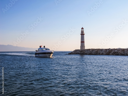 The boat sails to the shore near the lighthouse at sunset